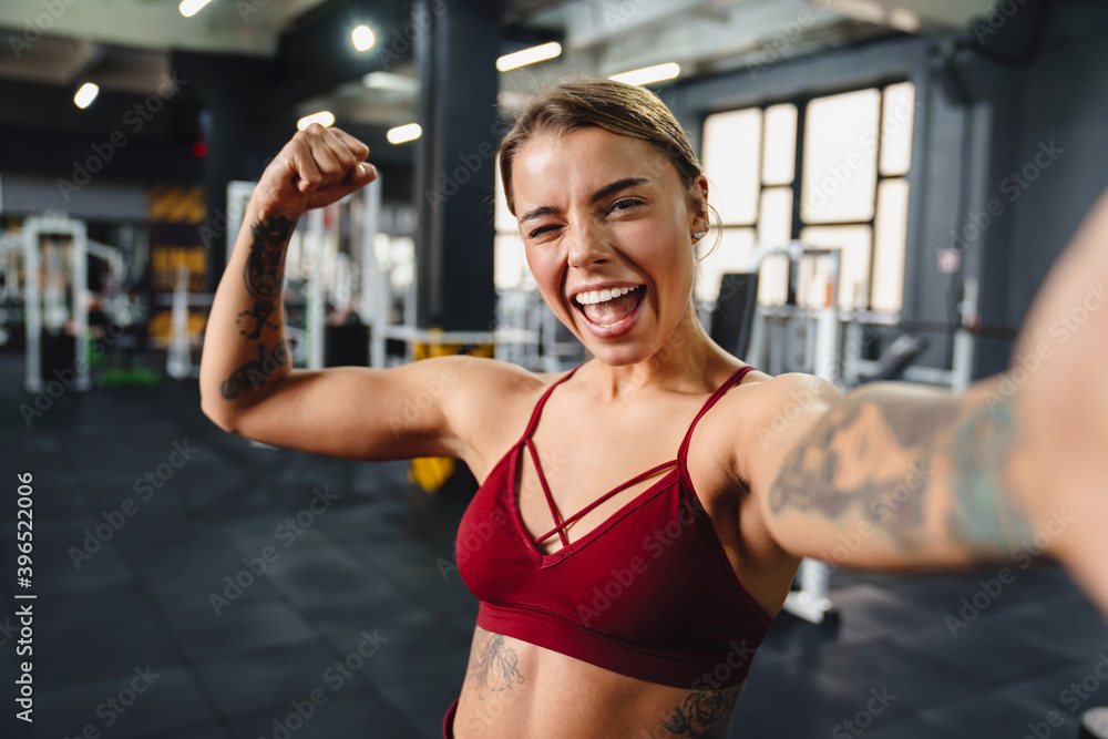 Excited sportswoman showing her bicep and winking while taking selfie Excited sportswoman showing her bicep and winking while taking selfie