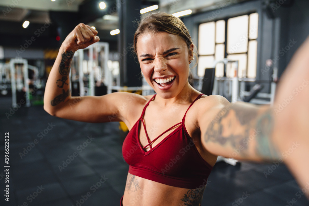Excited sportswoman showing her bicep and laughing while taking selfie