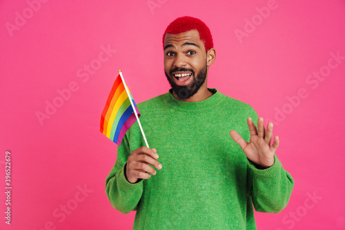 Joyful african american guy waving hand and holding rainbow flag