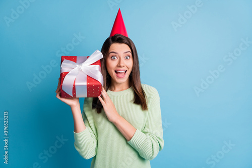Photo portrait of excited girl with open mouth holding present to ear listening shaking isolated on pastel blue colored background