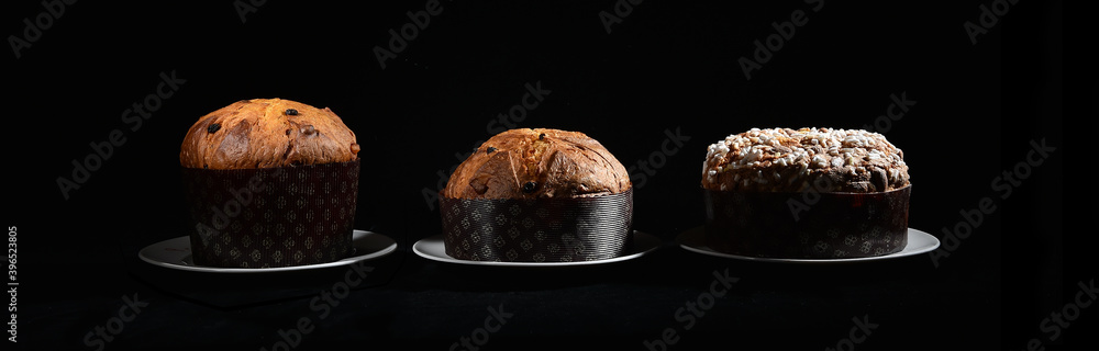 three types of Italian panettone: high, low and with almonds on a black background on a dish with cutting light - obrazy, fototapety, plakaty 