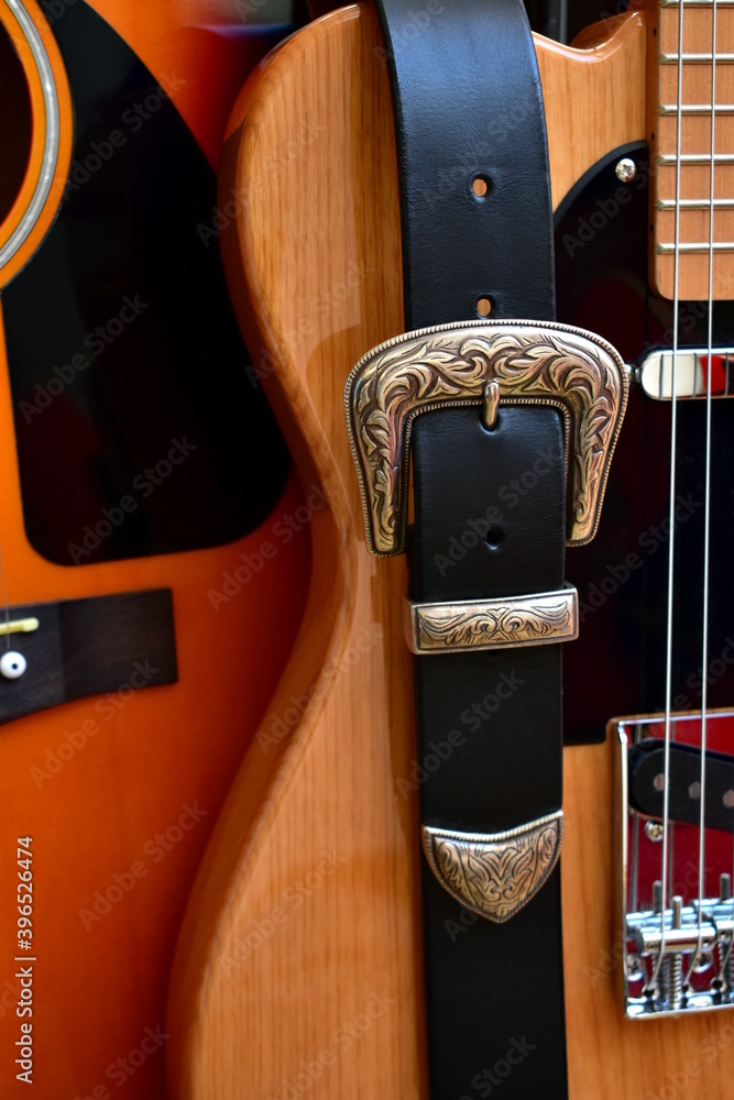 Acoustic and electric guitars and leather strap with silver buckle close-up.