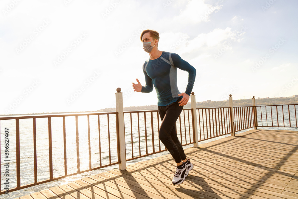 healthy and handsome young male model running on the beach. The man wearing a mask is running by the sea in sportswear. Healthy man who does sports outside with his mask due to corona virus measures.