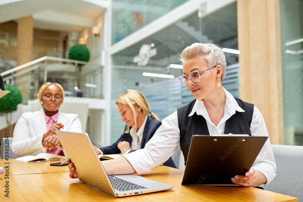 business lady working on laptop in office, while her diverse interracial group of partners colleagues work in the background. focus on woman, portrait business lady working on laptop in office, while her diverse interracial group of partners colleagues work in the background. focus on woman, portrait