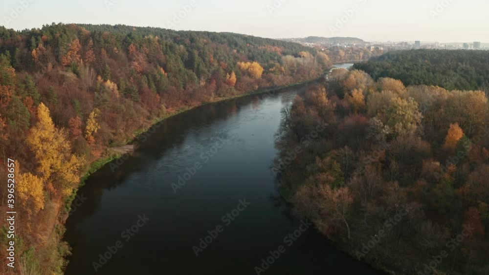 Drone flies over the river and autumn forest to the city in the distance. Drone flies over the river and autumn forest to the city in the distance.
