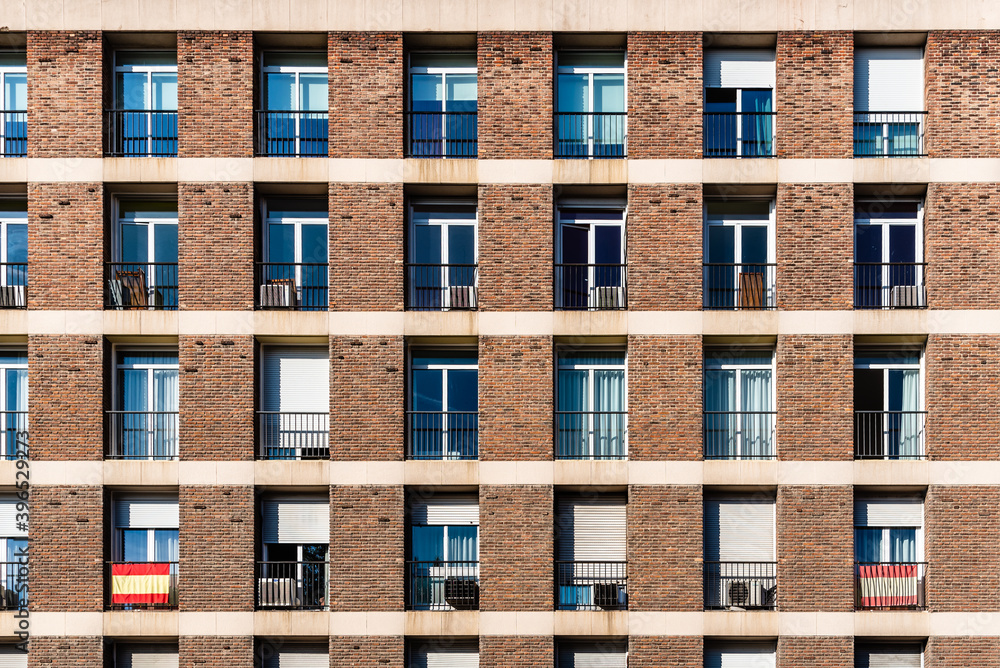 Full frame of brick facade of residential building with array of rectangular windows, some of them with Spanish flag