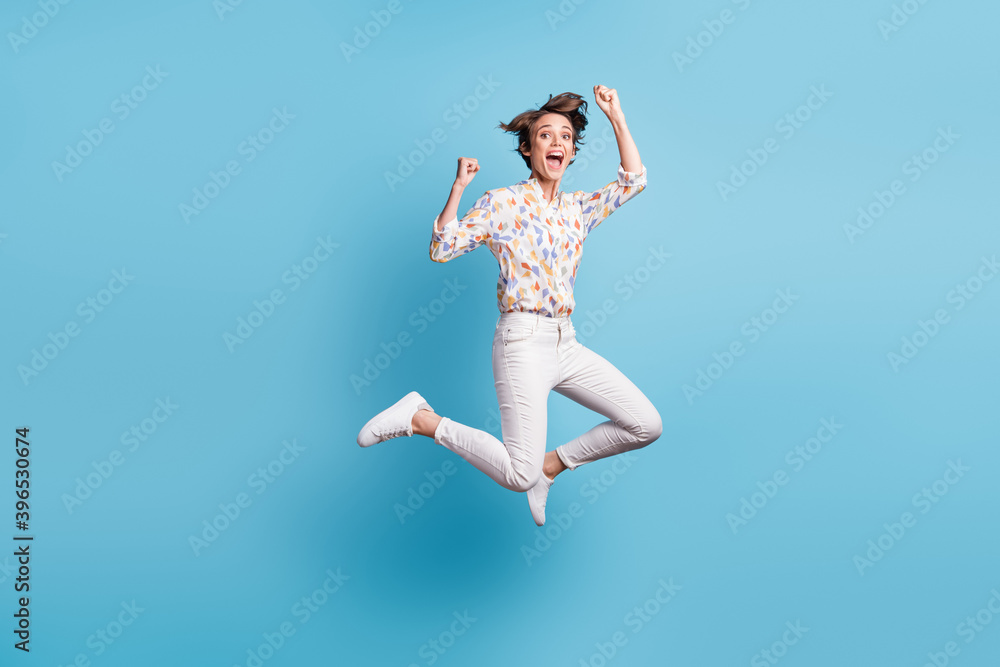 Full size photo of young crazy girl jump happy smile wow rejoice win victory goal fists hands isolated over blue color background Full size photo of young crazy girl jump happy smile wow rejoice win victory goal fists hands isolated over blue color background