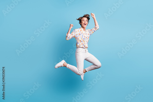 Full size photo of young crazy girl jump happy smile wow rejoice win victory goal fists hands isolated over blue color background