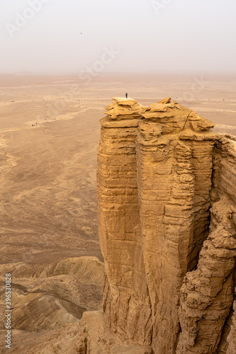 A person stands on a cliff overlooking the vast desert landscape at the Edge of the World in Saudi Arabia, a geological wonder with an uninterrupted view of the horizon