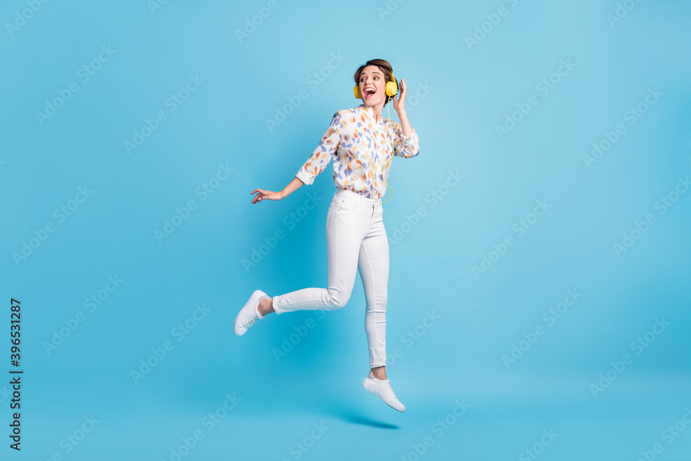 Full size photo of young girl happy positive smile jump look empty space listen music earphones isolated over blue color background
