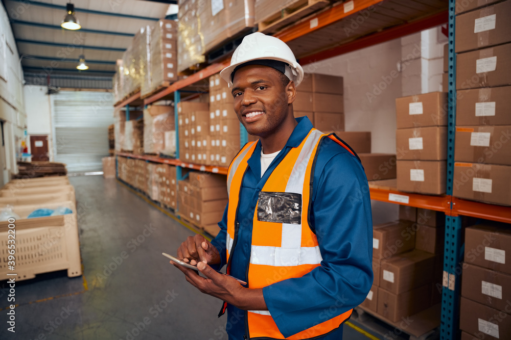 Smiling portrait of a african warehouse worker holding digital tablet in hand looking at camera Smiling portrait of a african warehouse worker holding digital tablet in hand looking at camera