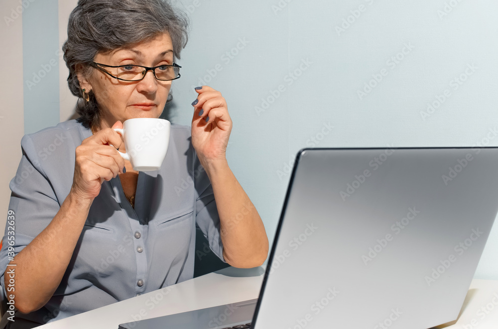 Elderly woman drinks coffee and looks surprised at laptop. Elderly woman drinks coffee and looks surprised at laptop.