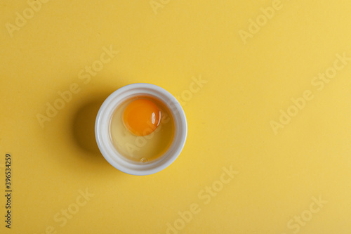 Raw egg in a bowl on a yellow background zenital view