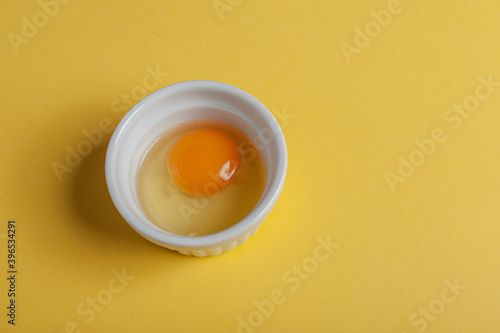 Raw egg in a bowl on a yellow background