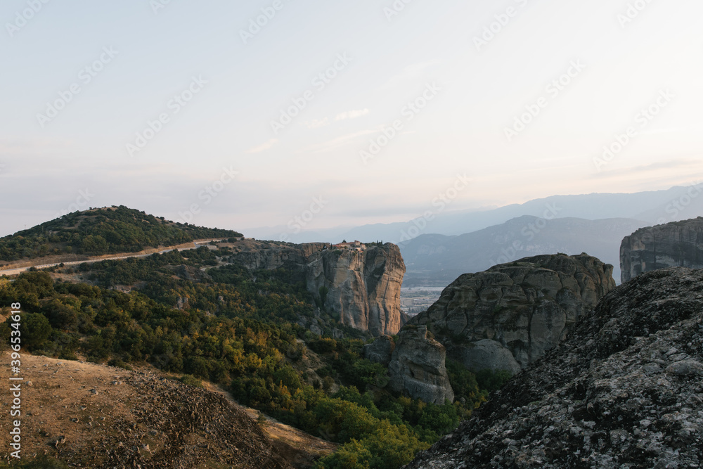 nature mountains and old monasteries buildings trees. cloudy skies europe greece on rock formation edge of cliff far away skyline