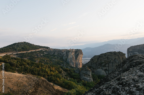nature mountains and old monasteries buildings trees. cloudy skies europe greece on rock formation edge of cliff far away skyline © Adam
