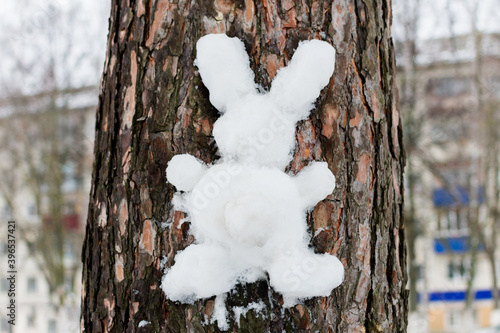 Bilde på lerret Handmade hare or rabbit made of white snow on the bark of a tree