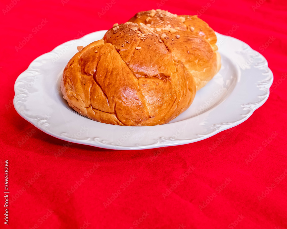 tsoureki, traditional Greek sweet bread served on white plate and red fabric background tsoureki, traditional Greek sweet bread served on white plate and red fabric background