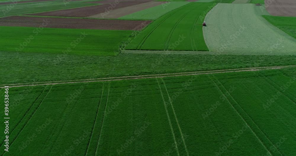 Aerial drone view of agriculture grassland field in summer. Tractor working on farming field. Farmer harvests crop. Descending, wide angle Aerial drone view of agriculture grassland field in summer. Tractor working on farming field. Farmer harvests crop. Descending, wide angle