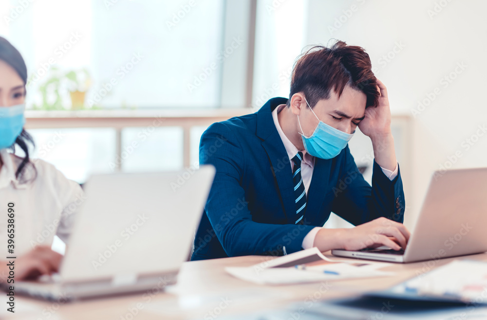 Stressed young business man wear face mask and working on laptop in office Stressed young business man wear face mask and working on laptop in office