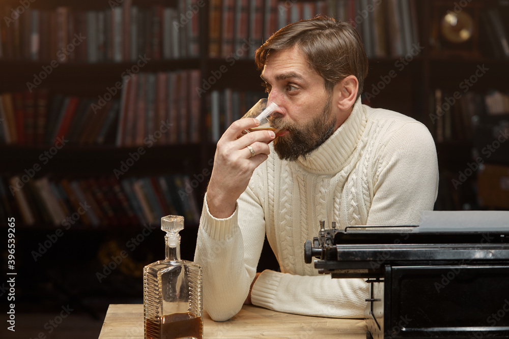 A thoughtful, concerned male writer working on a novel on a typewriter, drinking alcohol while thinking about solving a problem in the home office, a serious person looking for inspiration.