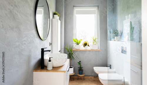 Grey bathroom with stylish sink  round mirror  window and toilet. Modern interior of spa with white furniture. Scandinavian design. 