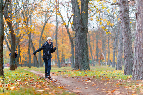 teen girl and boy running through the park and enjoys autumn, beautiful nature with yellow leaves
