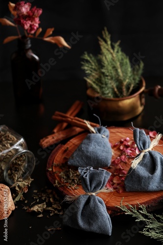 Yule winter solstice (Christmas) celebration themed magick spell bags made from blue cotton tied with yarn, filled with various herbs, spices. Dark black background with evergreens rose petals candles