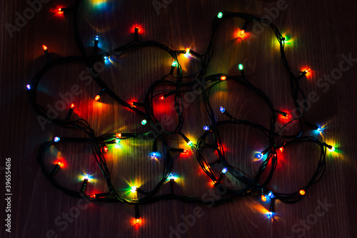Christmas garland on a wooden background. Bright multicolored bunch of holiday lights. Christmas lights at night on the table. The concept of approaching Christmas. Decorations for the Christmas tree.