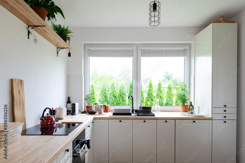 Stylish kitchen with white furniture, wooden counter and big window ...