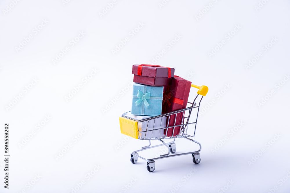 Miniature cart with gifts on a white background. Holidays shopping concept. Close-up.