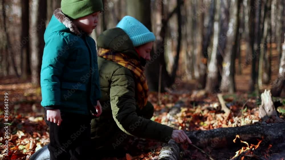 Young mother with little boy resting near autumn fire enjoying beautiful sunny magic forest. Family healthcare. Traveling lifestyle. Wild tourism. Weekend outside. Caucasian smiling male child. Young mother with little boy resting near autumn fire enjoying beautiful sunny magic forest. Family healthcare. Traveling lifestyle. Wild tourism. Weekend outside. Caucasian smiling male child.