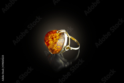 Gold ring with amber on black background illuminated by round light © Maria