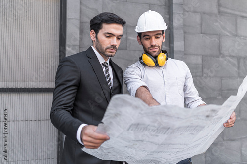 Project engineer and young businessman look plan blueprint together and discussing about new office building project.