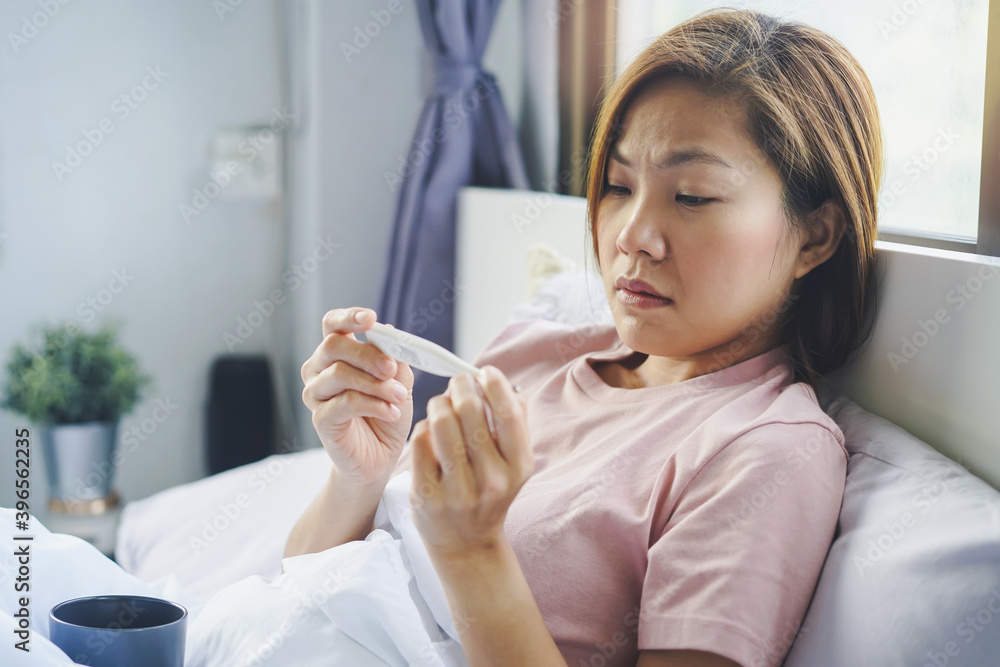 Cold and fever in winter. asian woman feeling sick and look at temperature on thermometer Cold and fever in winter. asian woman feeling sick and look at temperature on thermometer