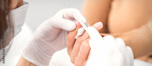 Close up of a manicurist files the female nails with the nail file in a nail salon