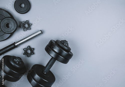 Φωτογραφία Top view of black dumbbells and different weight plates with barbell on grey background