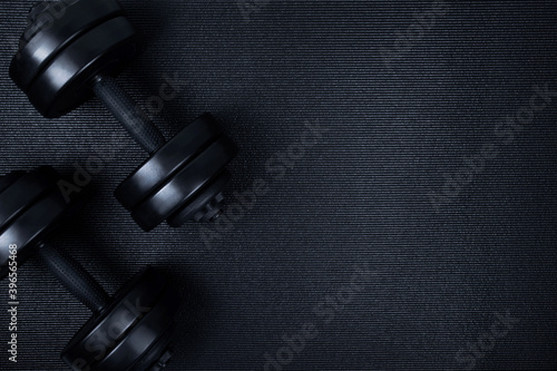 Top view of black dumbbells weights on textured mat background. Flat lay.