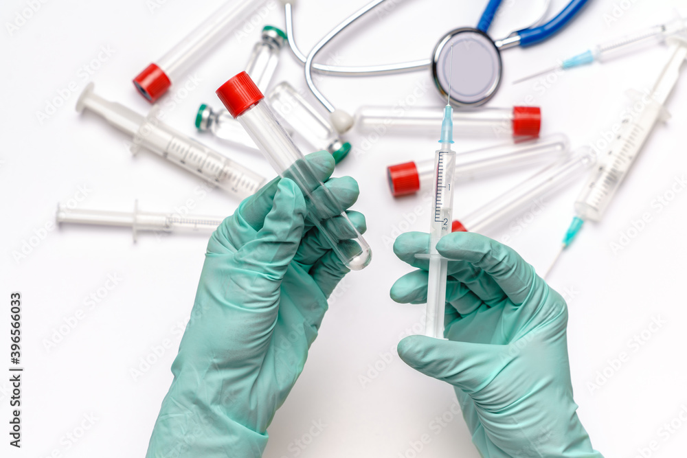 lab technician assistant holding syringe and test tube over light grey or white background with medical ampoule vials, syringes and stethoscope lab technician assistant holding syringe and test tube over light grey or white background with medical ampoule vials, syringes and stethoscope