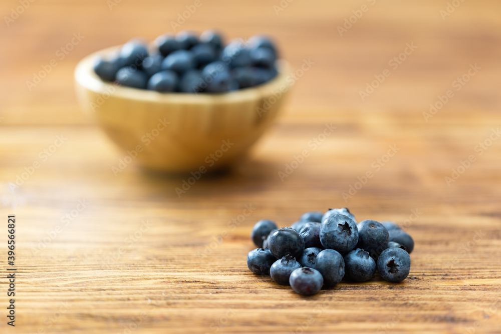 Pile of fresh blueberries laying on table with full bowl on background. Heap of little heatlthy ripe fruit on wooden table. Small raw berries rich in vitamin on brown desk. Pile of fresh blueberries laying on table with full bowl on background. Heap of little heatlthy ripe fruit on wooden table. Small raw berries rich in vitamin on brown desk.
