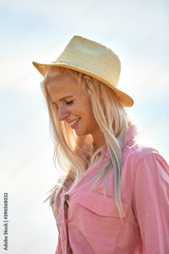Woman with long blond hair and a straw hat in a wheat field.