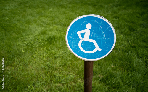 Small round parking lot wheelchair sign on green grass background.