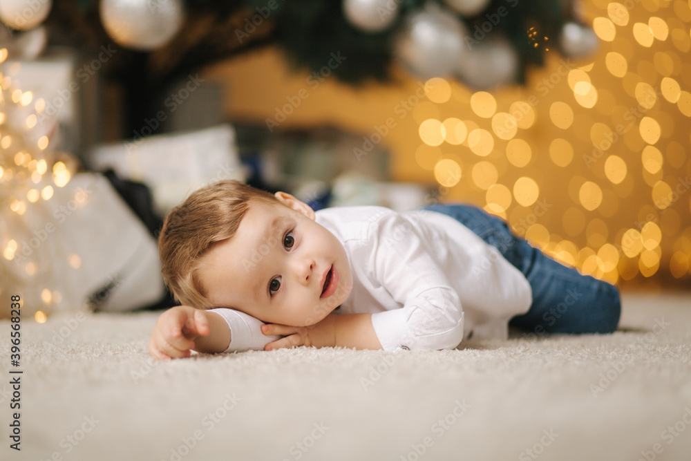 Cute little boy at home by the big Christmas tree looking for presents. Happy kid spend time on Holiday and enjoying every moment Cute little boy at home by the big Christmas tree looking for presents. Happy kid spend time on Holiday and enjoying every moment