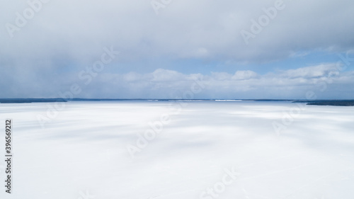 Aerial view of a white snowy lake and islands in winter on a sunny day, against a blue sky.