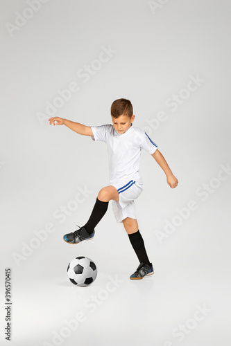 little child boy in uniform playing football over studio background. © producer