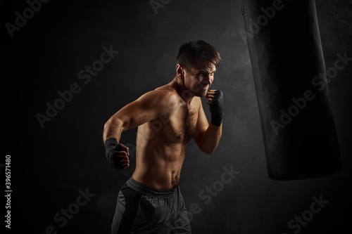 Male boxer training defense and attacks in boxing bag on black background © producer