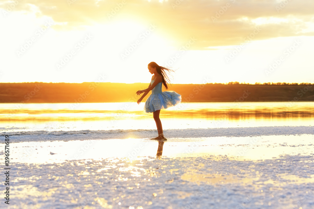 Young ballerina in the sunset light in the water of the lake. Silhouette of a young ballerina in a ballet dress in nature