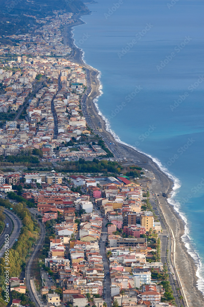the eastern coast of Sicily seen from above with its towns, roads, railways, buildings and highways on a partially covered autumn day