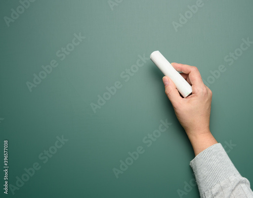 hand holds a piece of white chalk on the background of an empty green chalk board