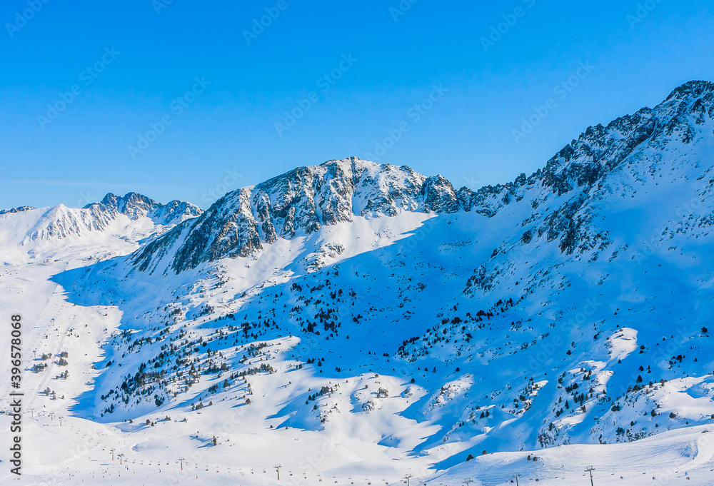 Beautiful mountain range covered in snow with clear sky on sunny day. Ski infrastructure and slopes in Pyrenees, Andorra